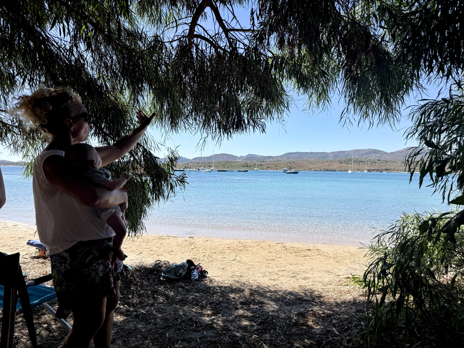 A parent holding a baby beside a calm sandy beach in northeast Sardinia