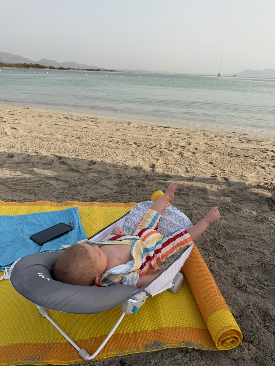 A baby resting in a shaded chair on a quiet sandy beach in northeast Sardinia